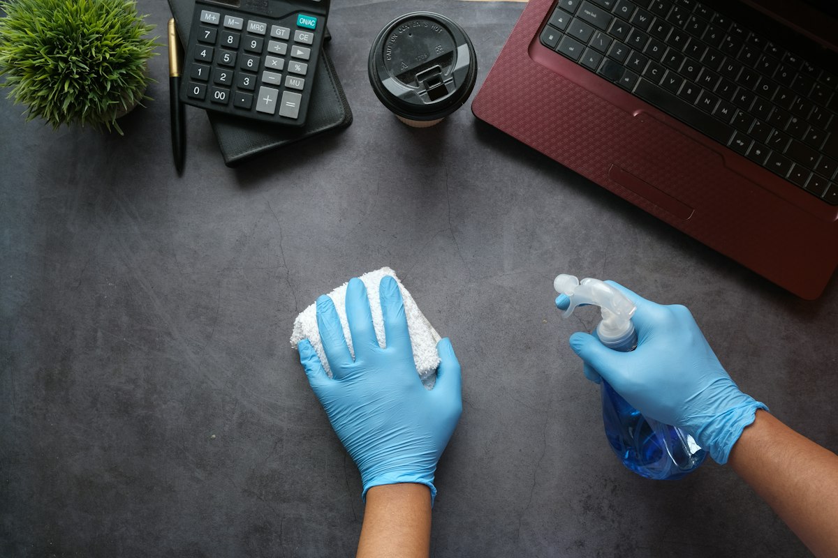 Gloved hands spraying and wiping a surface with disinfectant