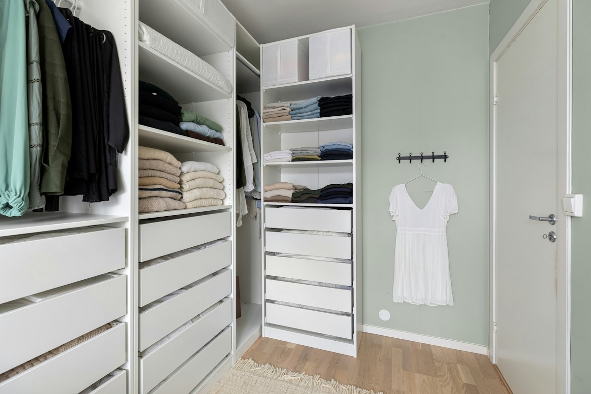Neatly organized white closet with folded sweaters and hanging clothes