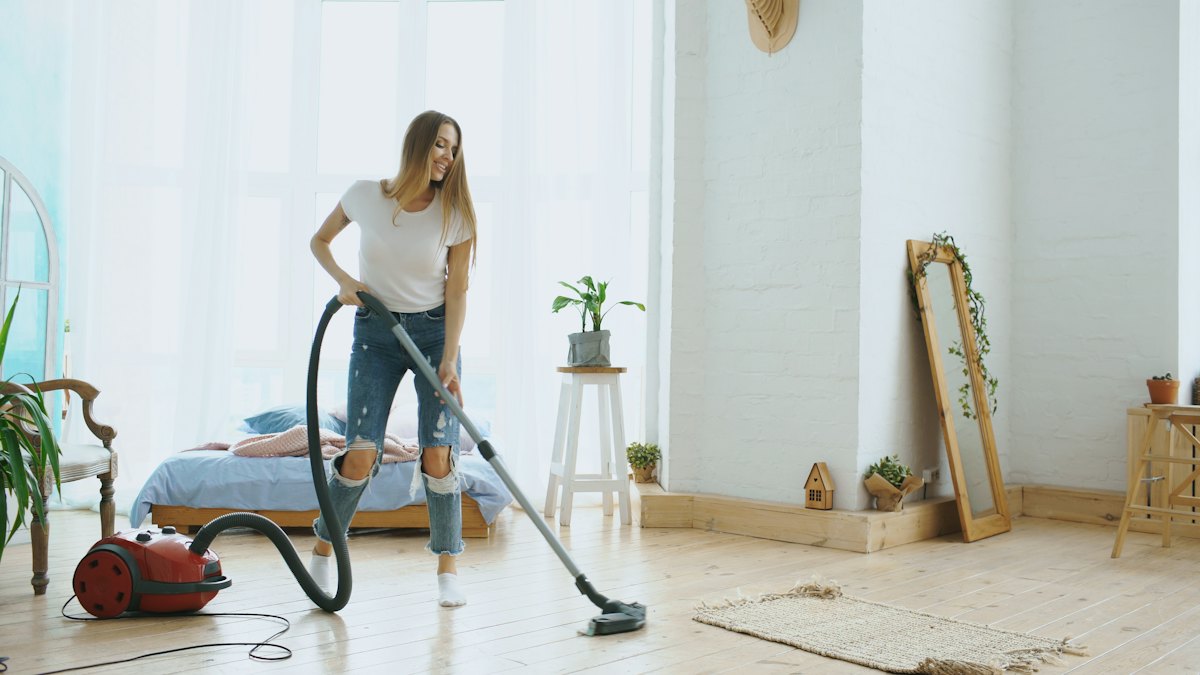 Cleaner vacuuming the hardwood floor of a bright living room